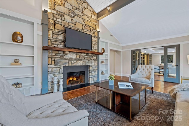 living room featuring a stone fireplace, wood finished floors, baseboards, built in features, and beamed ceiling