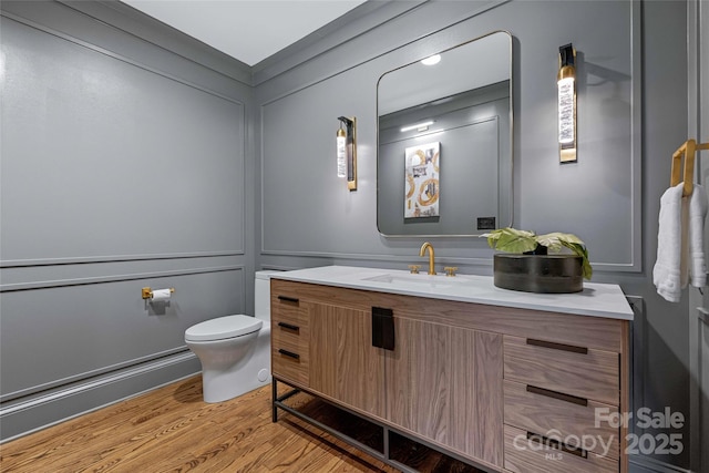 bathroom with a decorative wall, vanity, toilet, and wood finished floors