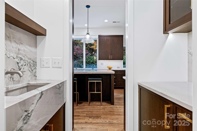 kitchen featuring light wood-style flooring, hanging light fixtures, dark brown cabinets, a sink, and recessed lighting