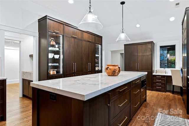 kitchen with visible vents, wood finished floors, light stone countertops, dark brown cabinets, and pendant lighting