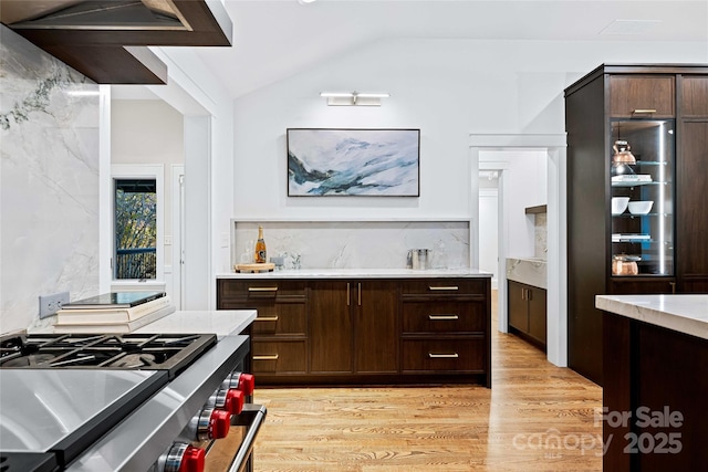 bar with lofted ceiling, light wood-style flooring, stainless steel range, and backsplash