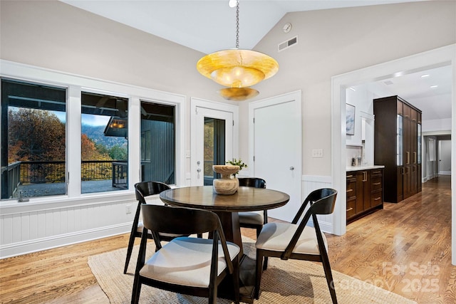 dining space featuring lofted ceiling, visible vents, light wood-style flooring, and a wainscoted wall