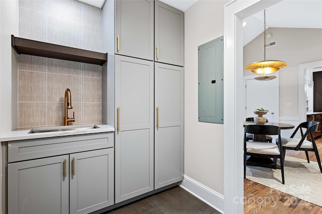 kitchen featuring gray cabinets, light countertops, vaulted ceiling, a sink, and electric panel