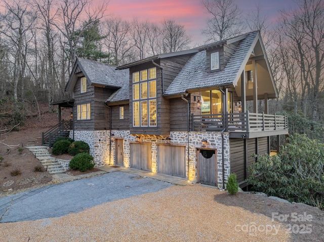 chalet / cabin with a garage, stone siding, driveway, and stairway