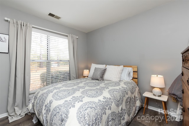 bedroom with baseboards, visible vents, and wood finished floors