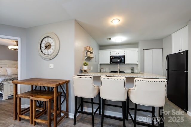 kitchen with a peninsula, black appliances, white cabinets, and backsplash