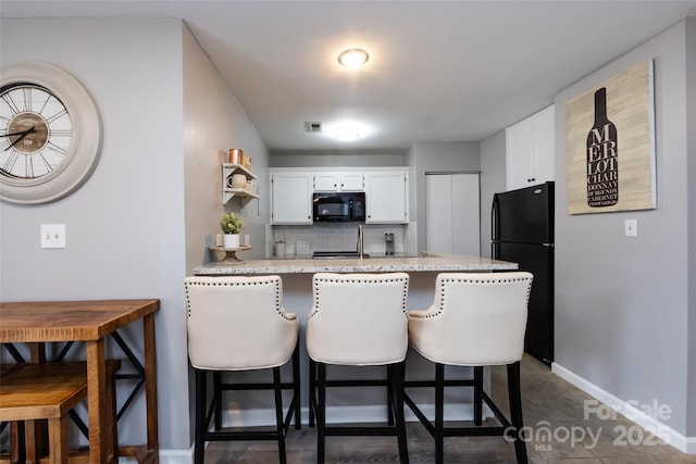 kitchen with a peninsula, white cabinetry, a kitchen breakfast bar, backsplash, and black appliances