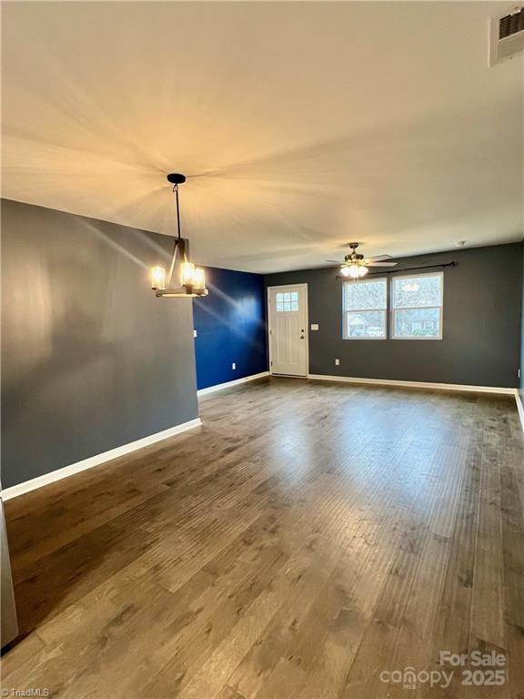 interior space featuring ceiling fan with notable chandelier, wood finished floors, visible vents, and baseboards