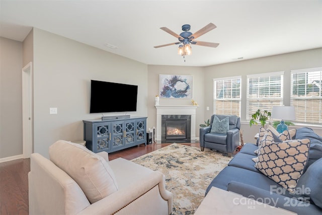 living room with ceiling fan, a tile fireplace, wood finished floors, and baseboards