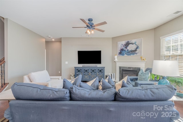 living room featuring a glass covered fireplace, visible vents, ceiling fan, and wood finished floors