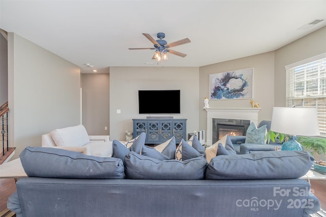 living room featuring ceiling fan, wood finished floors, a glass covered fireplace, and visible vents