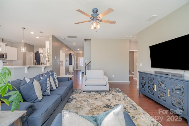 living room with arched walkways, ceiling fan, baseboards, stairs, and dark wood-style floors