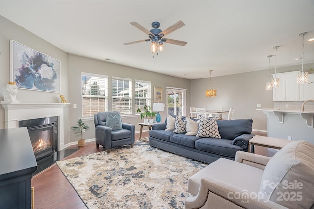 living room with visible vents, baseboards, a ceiling fan, a glass covered fireplace, and wood finished floors