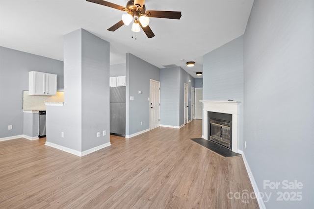 unfurnished living room with light wood finished floors, a fireplace with flush hearth, a ceiling fan, and baseboards