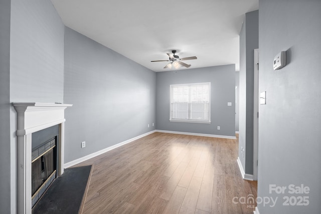 unfurnished living room with a ceiling fan, a glass covered fireplace, baseboards, and wood finished floors