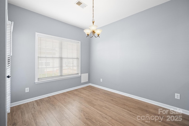 empty room with a chandelier, visible vents, baseboards, and wood finished floors