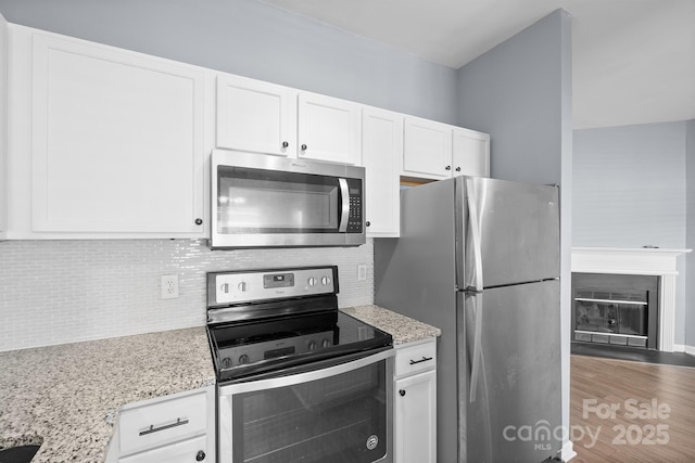 kitchen featuring stainless steel appliances, white cabinetry, light stone counters, and tasteful backsplash