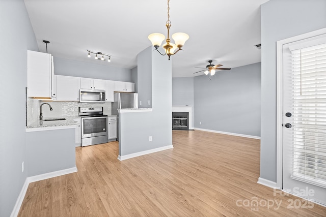 kitchen featuring ceiling fan with notable chandelier, stainless steel appliances, a fireplace, a sink, and light wood-style floors