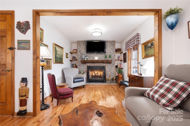 sitting room with a large fireplace, baseboards, and wood finished floors