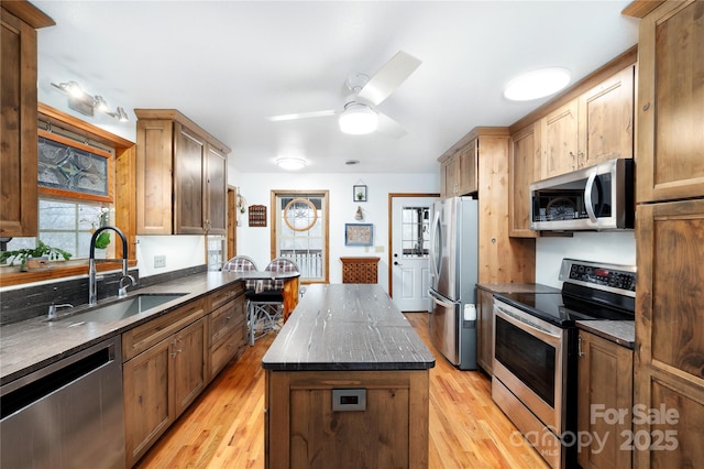 kitchen with appliances with stainless steel finishes, a kitchen island, light wood-type flooring, and a sink