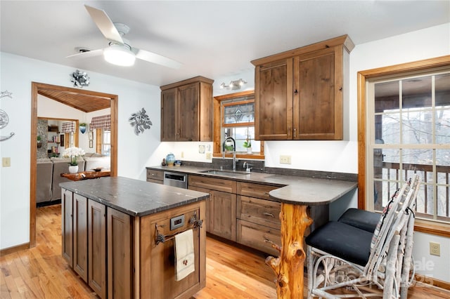 kitchen featuring a sink, a kitchen island, light wood-style flooring, a ceiling fan, and stainless steel dishwasher