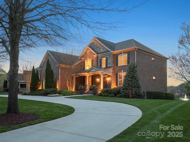 colonial inspired home with a yard, brick siding, and curved driveway