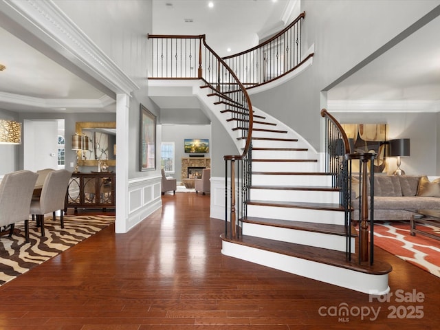 foyer featuring a decorative wall, a stone fireplace, a wainscoted wall, stairway, and wood finished floors