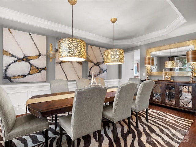 dining room featuring crown molding, a wainscoted wall, a tray ceiling, a decorative wall, and wood finished floors