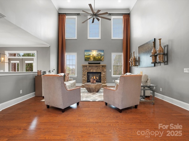 living area with ornamental molding, a stone fireplace, a ceiling fan, and wood finished floors