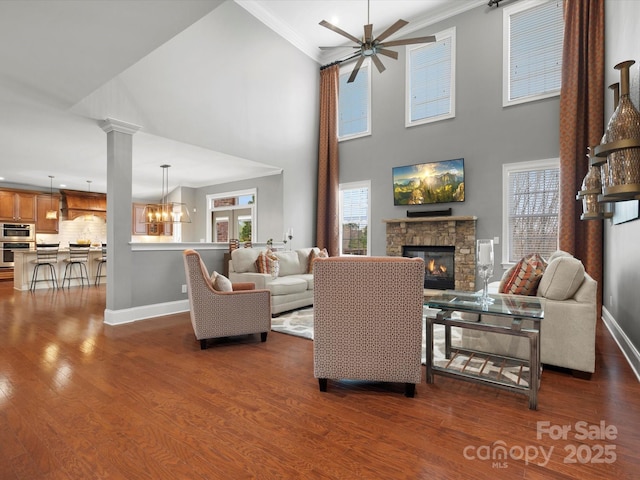 living room featuring baseboards, a fireplace, crown molding, dark wood-style floors, and ceiling fan with notable chandelier