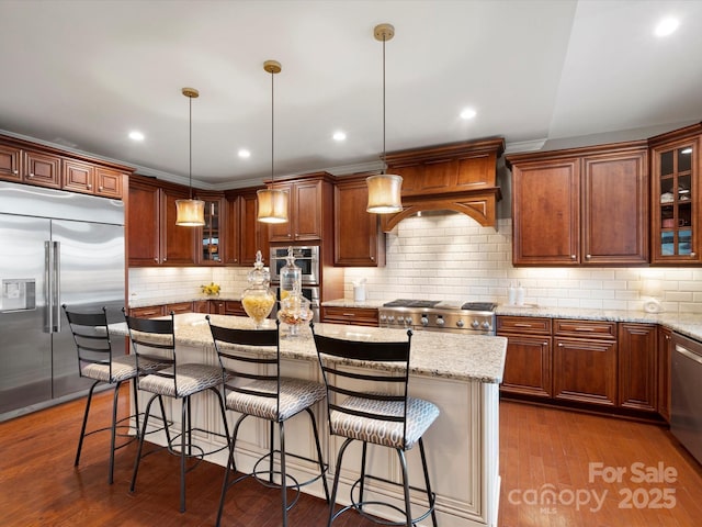 kitchen with dark wood finished floors, glass insert cabinets, light stone countertops, a kitchen island, and stainless steel appliances