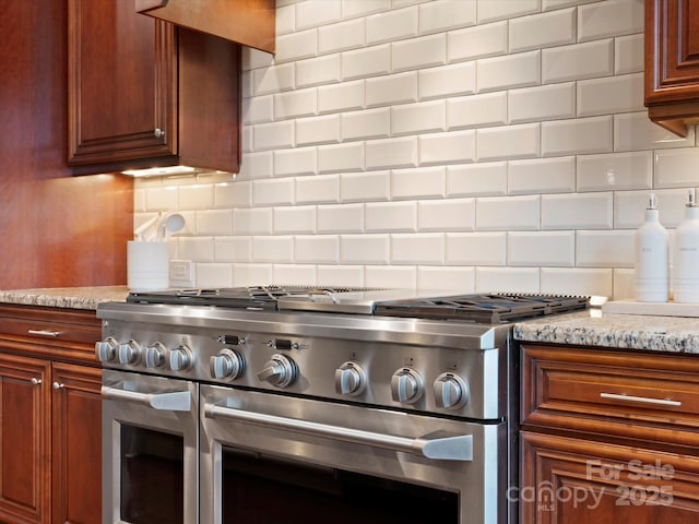 kitchen featuring backsplash, range with two ovens, and light stone countertops