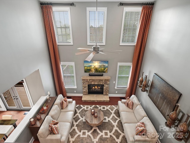 living room featuring a towering ceiling, baseboards, a fireplace, ceiling fan, and wood finished floors