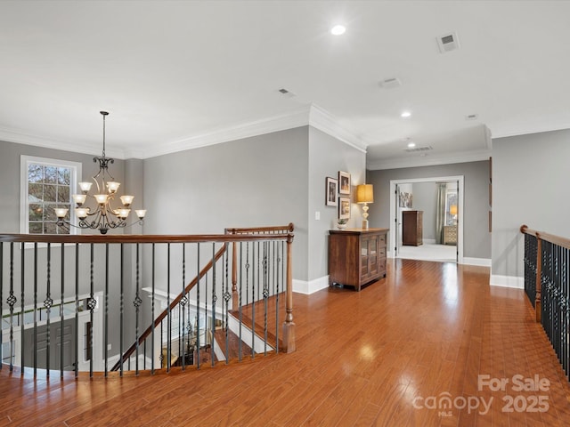 hall with visible vents, baseboards, an upstairs landing, a chandelier, and wood finished floors