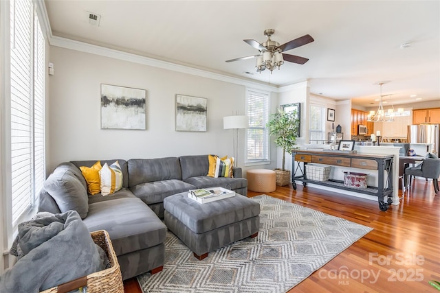 living area featuring crown molding, visible vents, wood finished floors, and ceiling fan with notable chandelier