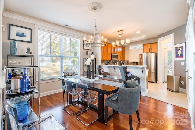 dining area with baseboards, wood finished floors, visible vents, and a notable chandelier