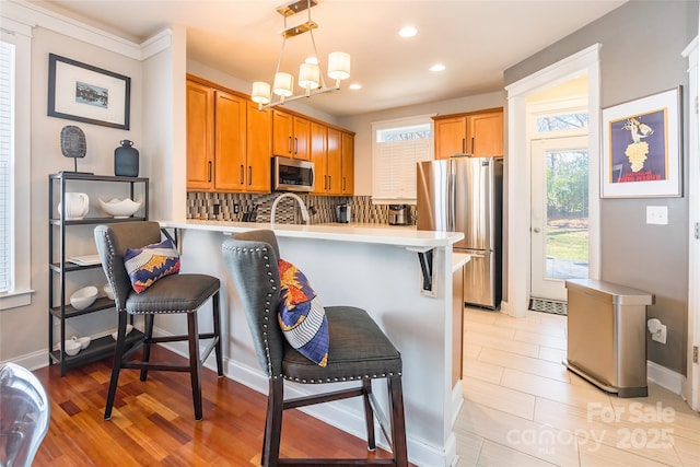 kitchen with decorative backsplash, a kitchen breakfast bar, a peninsula, stainless steel appliances, and light countertops