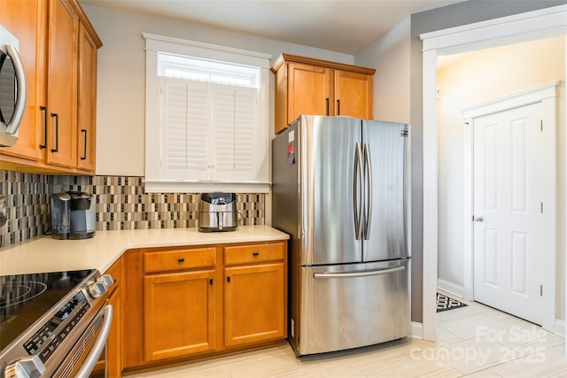 kitchen with brown cabinetry, freestanding refrigerator, light countertops, and backsplash