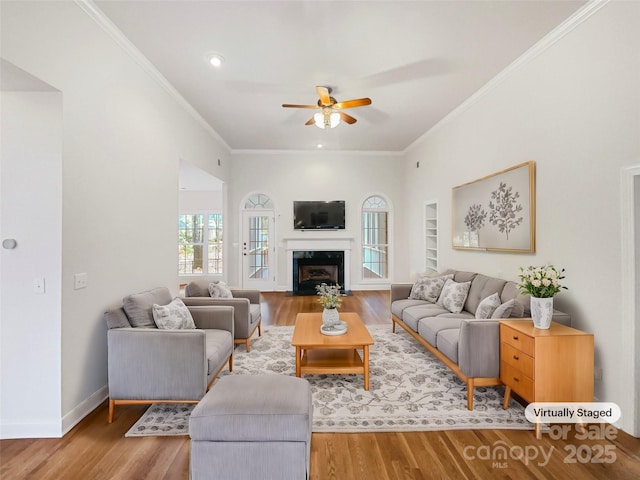 living room with built in features, crown molding, a fireplace with flush hearth, wood finished floors, and baseboards