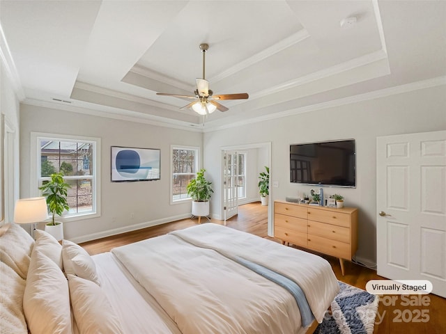 bedroom with ornamental molding, wood finished floors, and a raised ceiling