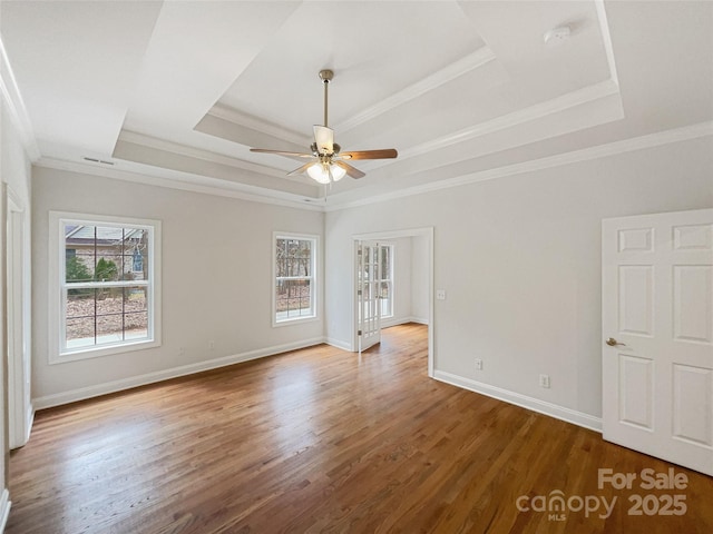 empty room featuring a raised ceiling, ornamental molding, a ceiling fan, wood finished floors, and baseboards