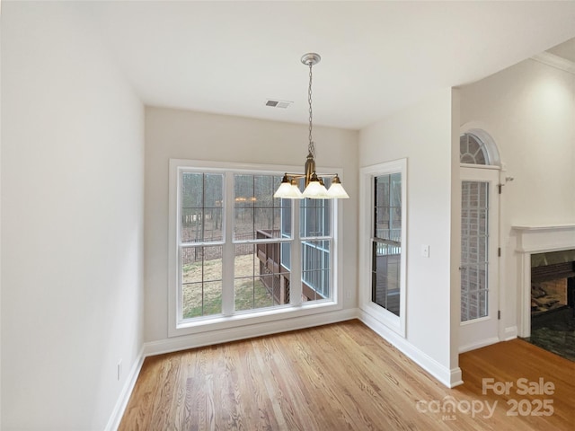 unfurnished dining area with baseboards, a premium fireplace, visible vents, and wood finished floors