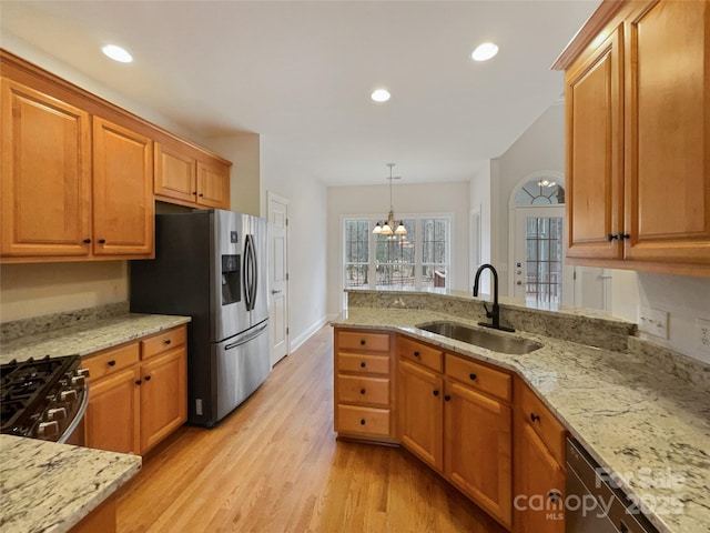 kitchen with stainless steel appliances, light stone counters, a sink, and light wood-style floors