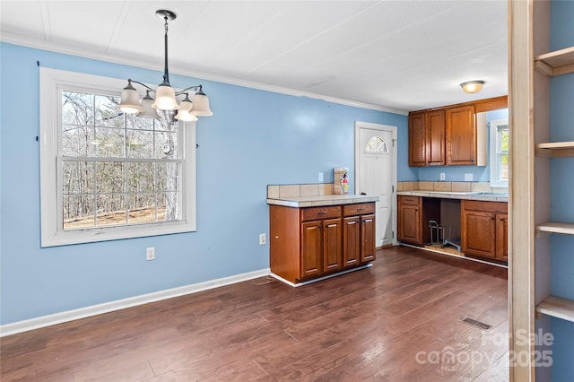 kitchen with dark wood-style floors, tile counters, brown cabinets, and ornamental molding