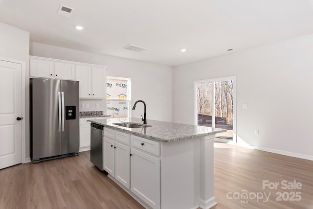 kitchen featuring white cabinets, light stone countertops, stainless steel appliances, light wood-type flooring, and a sink