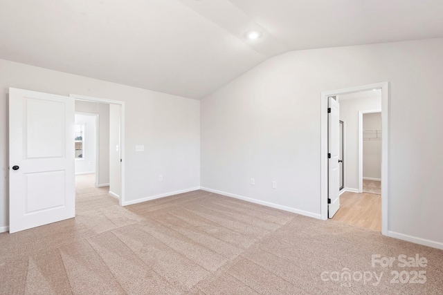 unfurnished room featuring lofted ceiling, baseboards, and light colored carpet