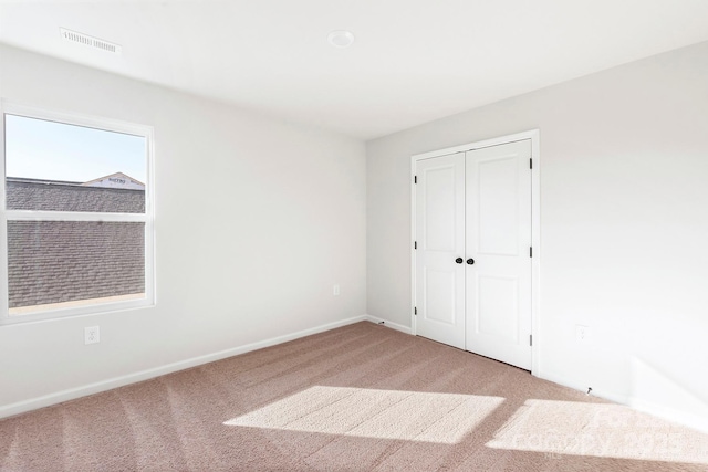 unfurnished bedroom with a closet, visible vents, light carpet, and baseboards