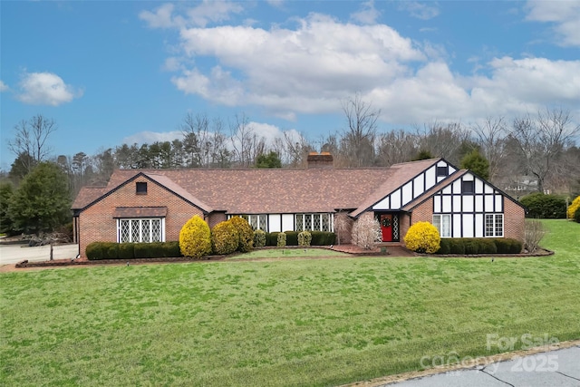 view of front facade with brick siding, a chimney, a front yard, and a shingled roof