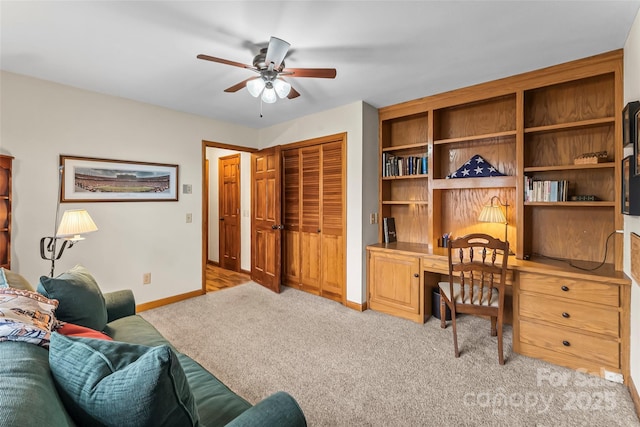 home office with light carpet, built in desk, a ceiling fan, and baseboards