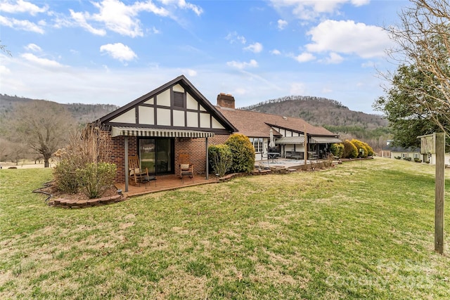 back of house featuring a patio, a mountain view, brick siding, a lawn, and a chimney